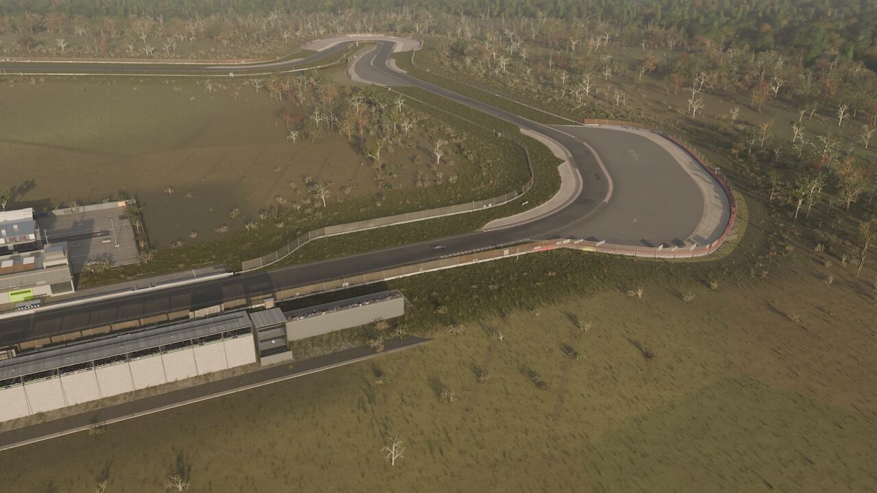 The closing wide: the circuit sweeping away below with pit buildings and treeline, late afternoon light.